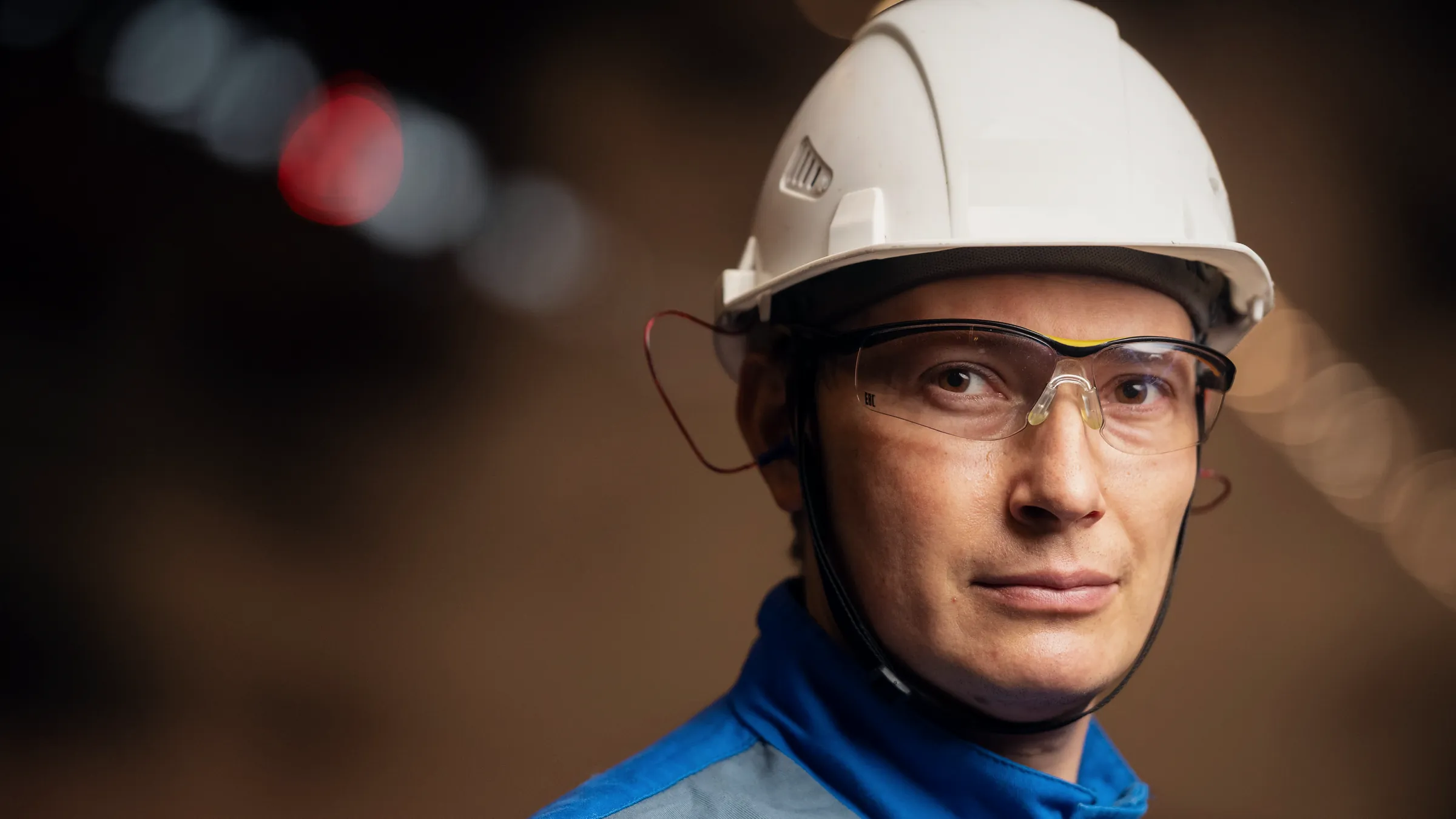 An engineer in a white hard hat and clear safety glasses, looking at the camera